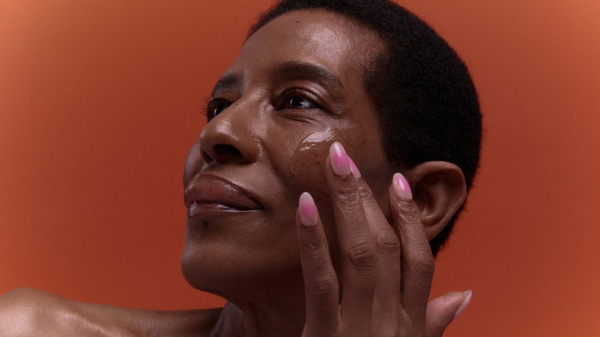 Image contains a model applying a face oil on bare skin.